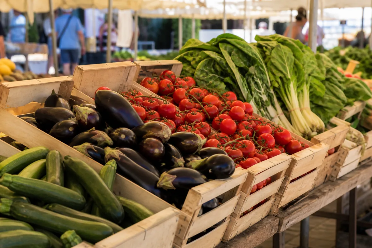 Cageots de légumes de saison alignés sur un étal de marché en plein soleil